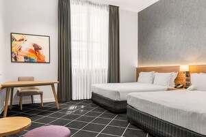 Hotellihuone, jossa on kaksi sänkyä, työpöytä, tuoli ja taulu seinällä.