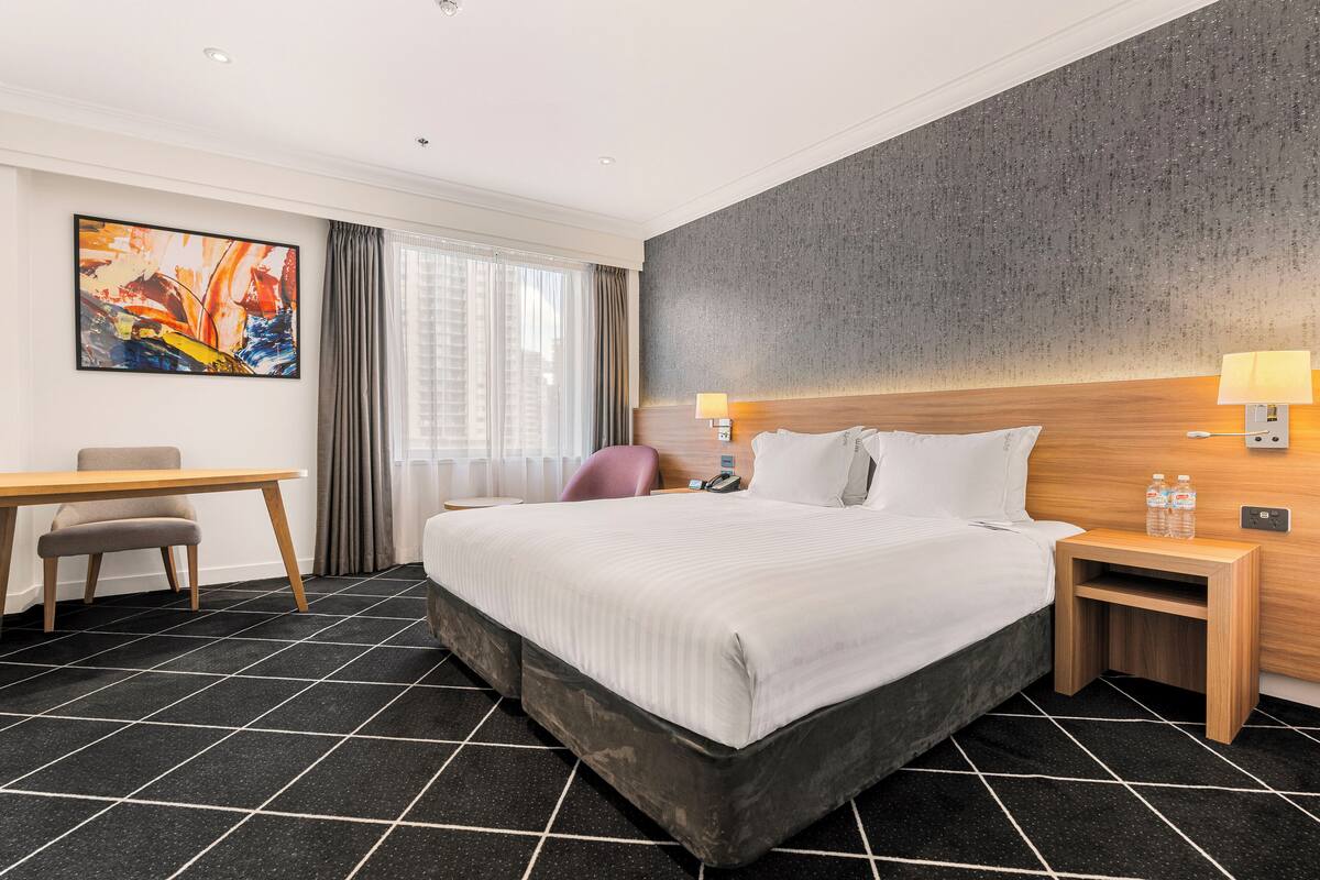 Ein Hotelzimmer mit einem großen Bett, einem Schreibtisch, einem Stuhl, einem Nachttisch mit Lampe und einem Bild an der Wand.