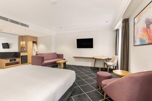 Une chambre d’hôtel avec un lit, un canapé, un bureau, une chaise, une télévision et un tableau au mur.
