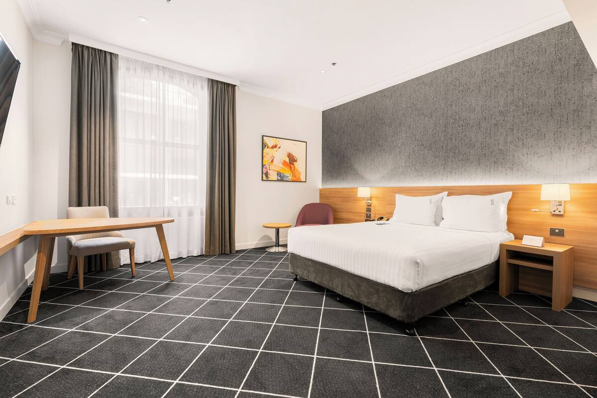 Ein Hotelzimmer mit einem großen Bett, einem Schreibtisch, einem Stuhl und einem kleinen Tisch.