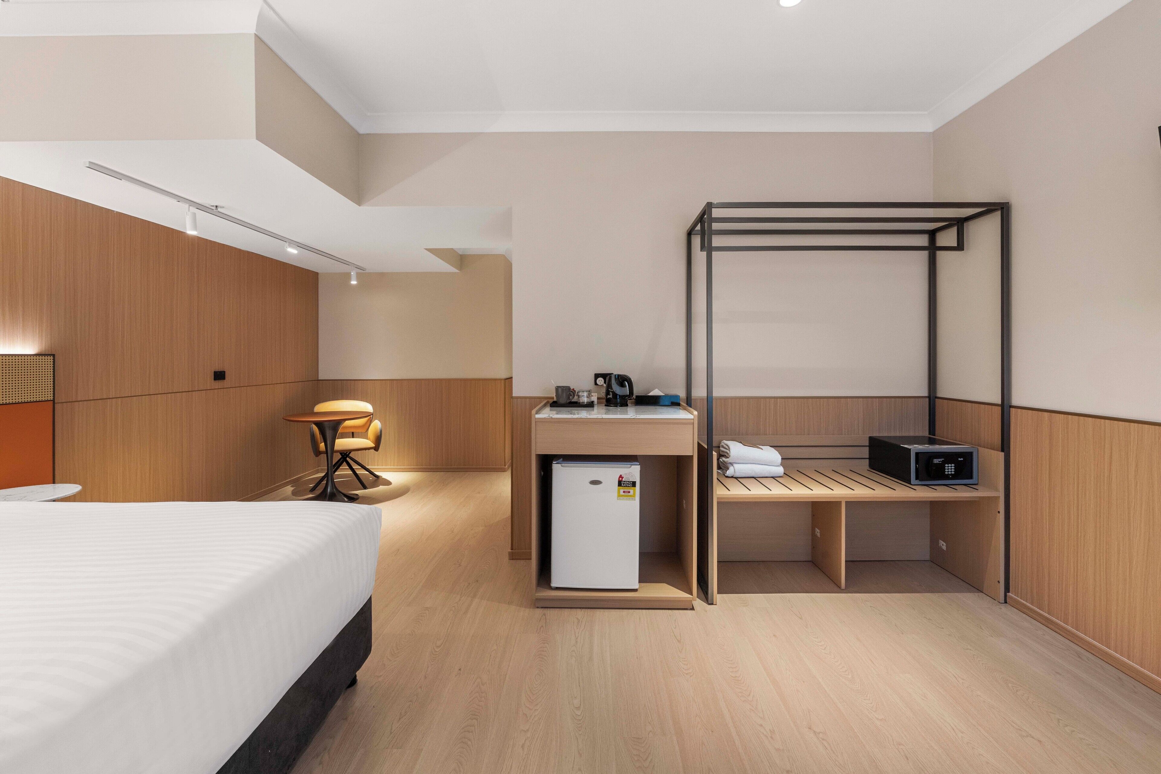 A modern hotel room with a bed, desk, chair, and a small refrigerator.