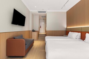Una habitación de hotel moderna con sofá, cama, televisor montado en la pared y una escalera que lleva a otra habitación.