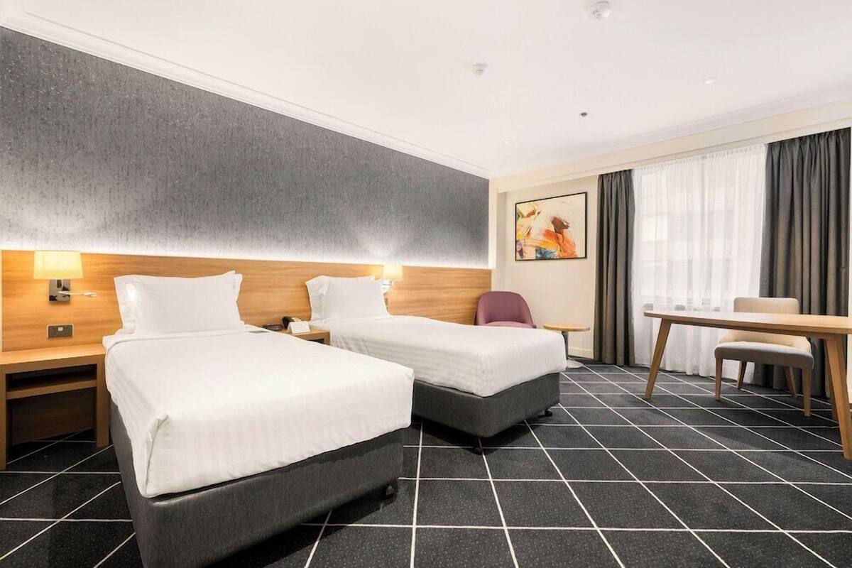 Ein Hotelzimmer mit zwei Betten, einem Schreibtisch und einem Stuhl.