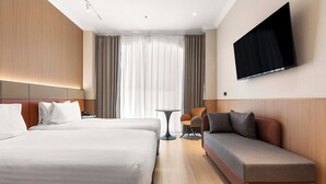 Habitación de hotel con dos camas, un sofá, un televisor y una pequeña mesa.