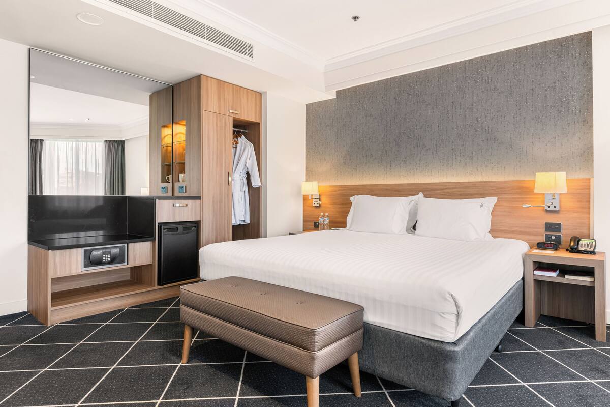 Ein modernes Hotelzimmer mit einem großen Bett, einem Flachbildfernseher, einer Minibar, einem Holzschrank und einer Bank.