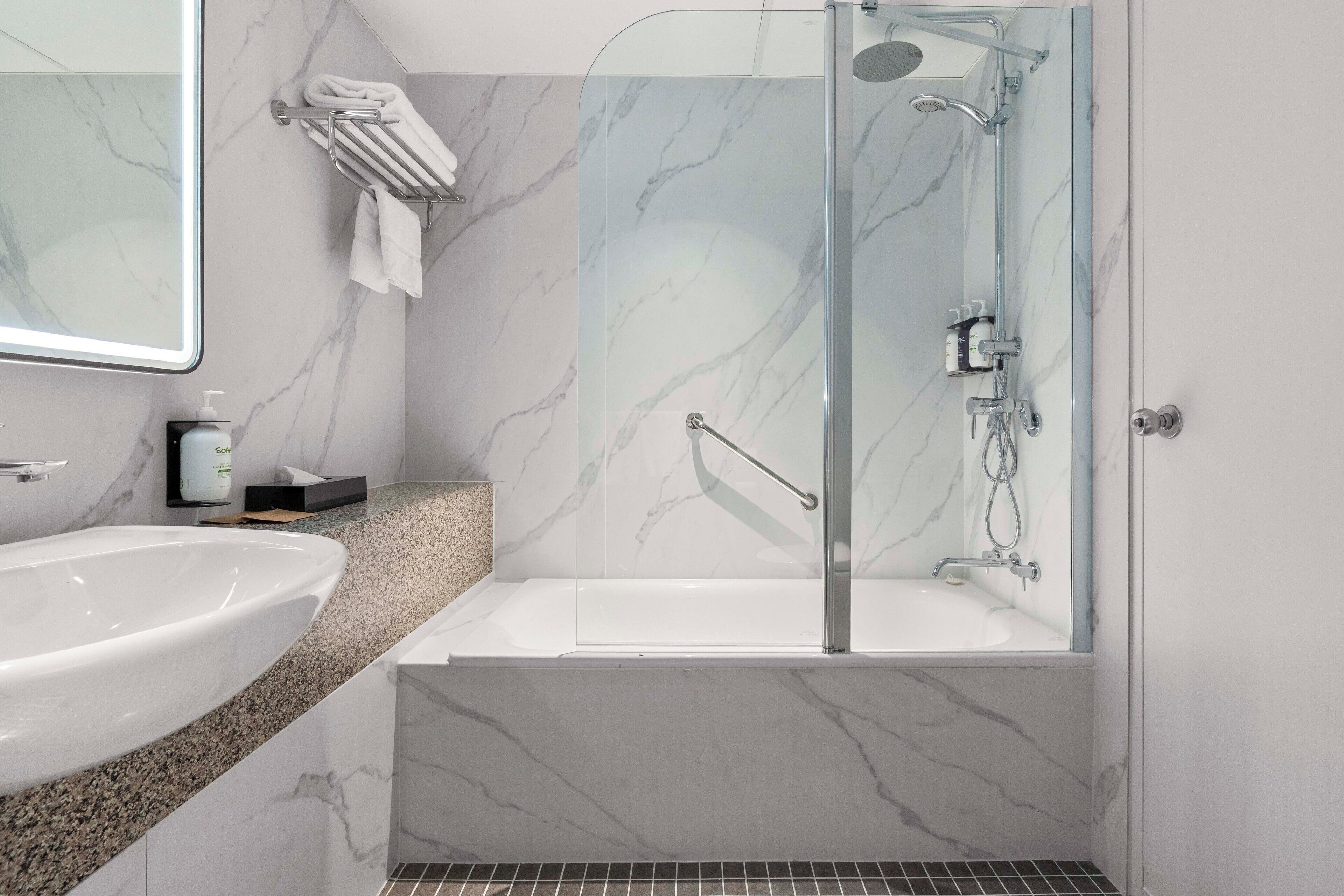 A modern bathroom with a marble sink, a glass-enclosed shower, and a large mirror.