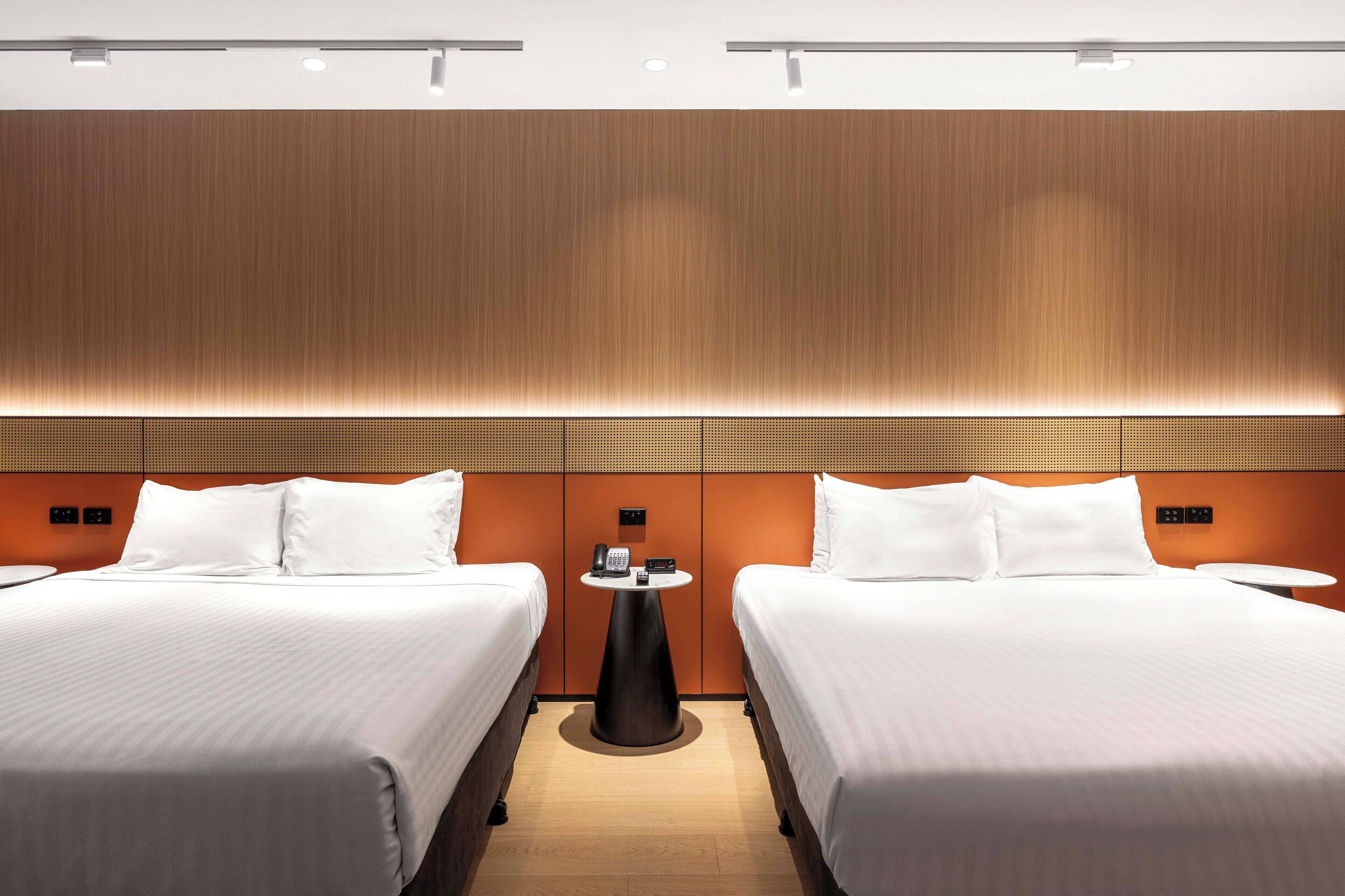 Quarto de hotel com duas camas, uma mesa pequena e um telefone fixado na parede.