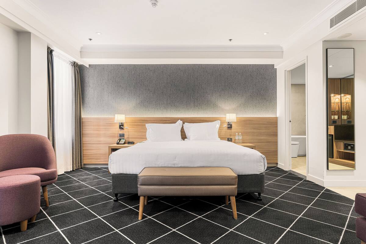 Ein modernes Hotelzimmer mit einem großen Bett, einem Nachttisch, einem Sessel und einem Spiegel.