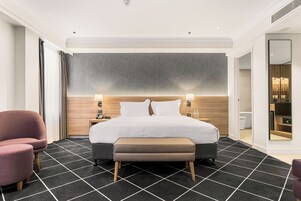 Moderni hotellihuone, jossa on suuri sänky, yöpöytä, tuoli ja peili.