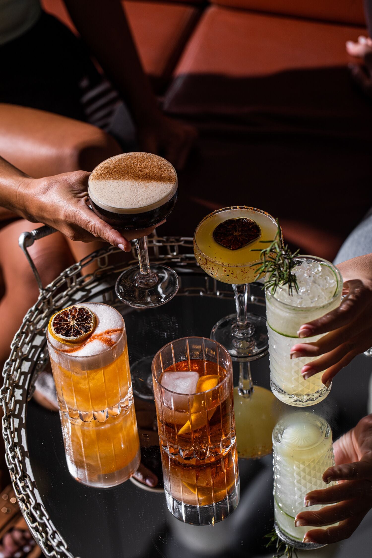 Una bandeja con diversas bebidas, incluyendo un cóctel con espuma, un vaso con una rodaja de fruta deshidratada y un vaso con hielo y una ramita de romero.