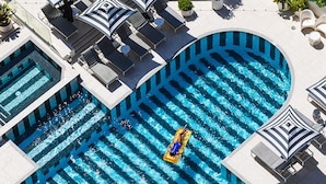 A large, curved swimming pool with multiple lanes, surrounded by lounge chairs and umbrellas.