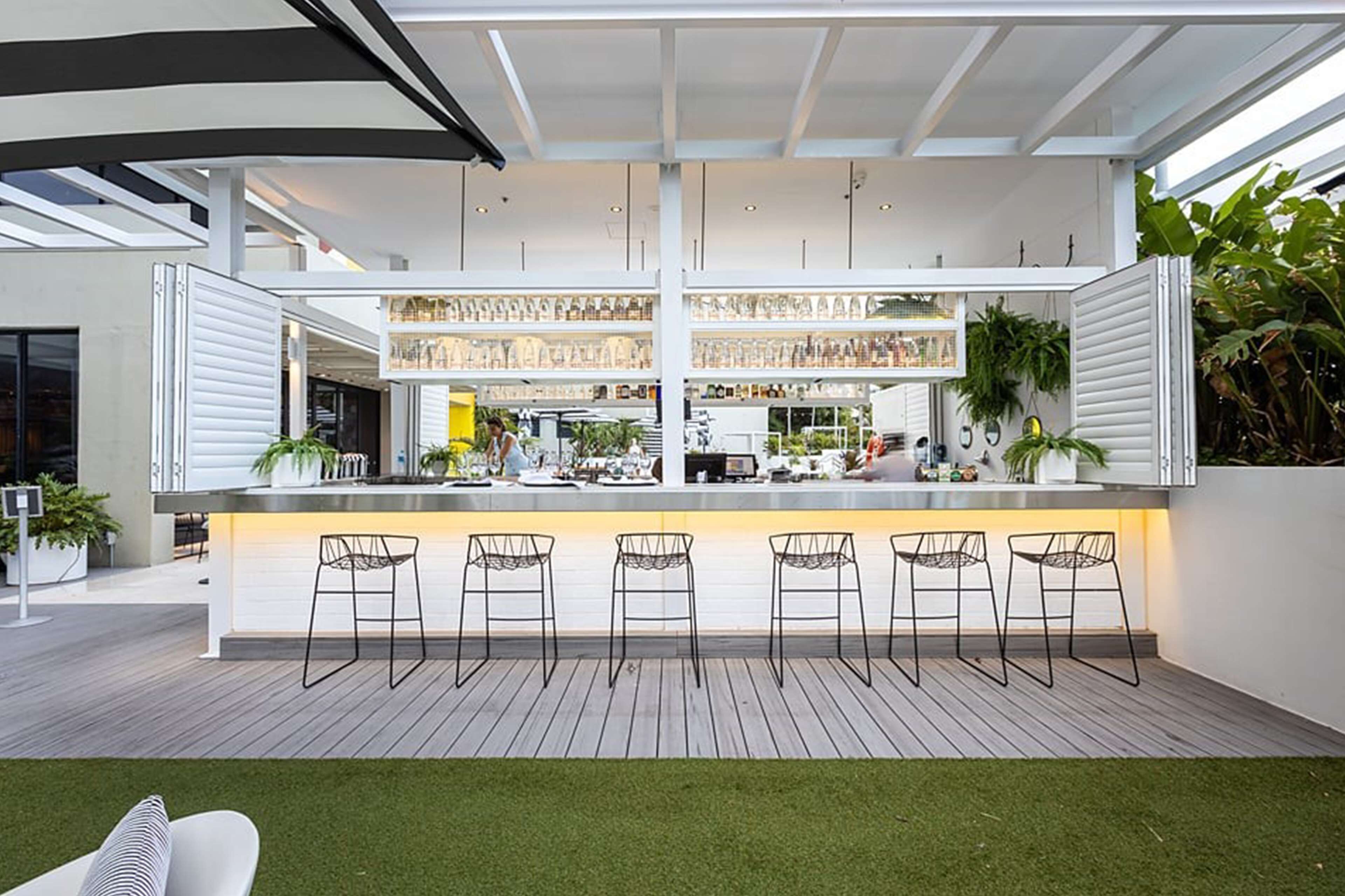 A modern bar area with a central island, bar stools, and shelves stocked with bottles.