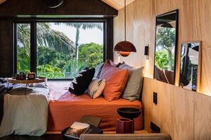 Un dormitorio acogedor con un ventanal grande, una cama con muchas almohadas, una mesita de noche con una bandeja y una pared de madera.