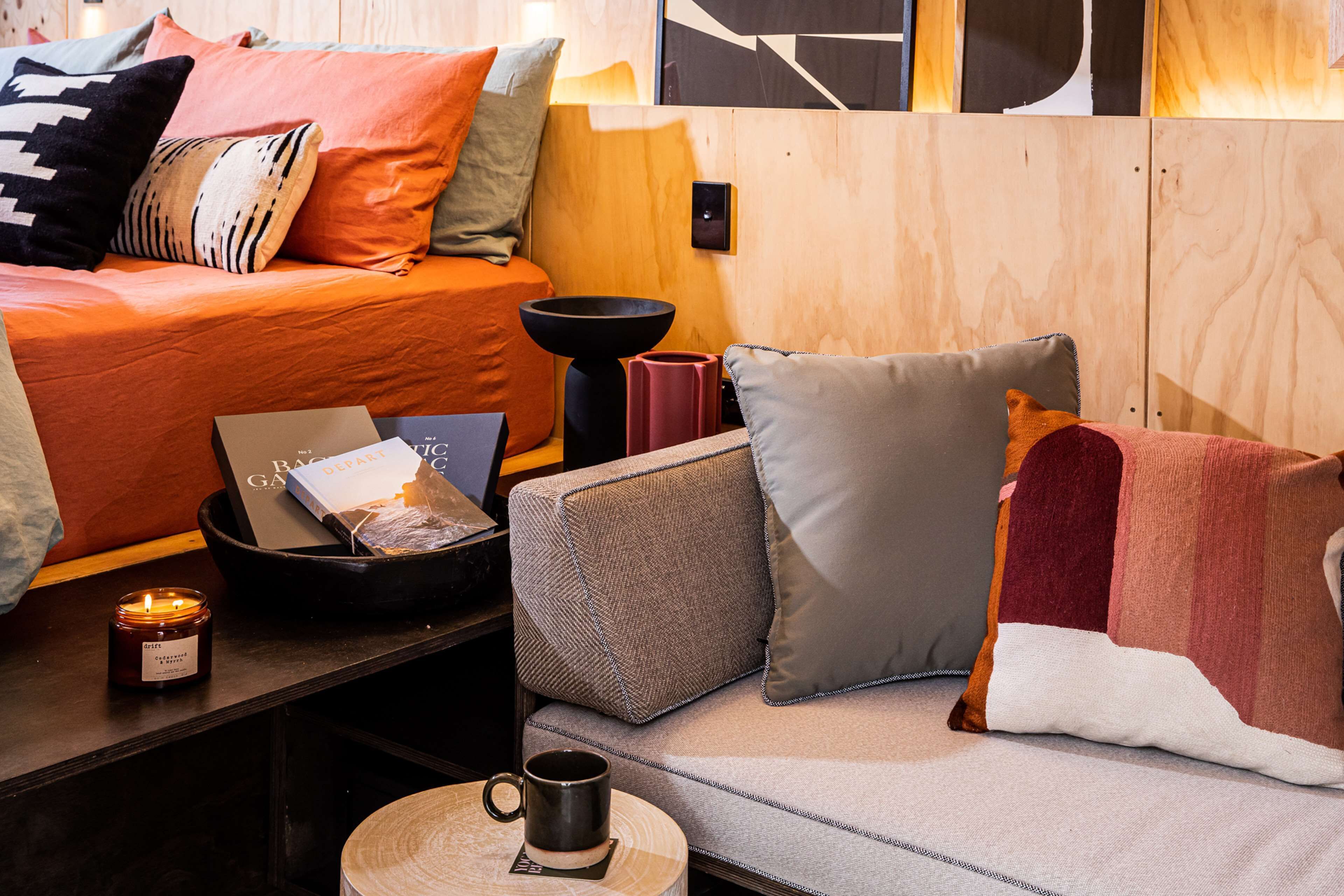 Una habitación acogedora con cama, sofá, mesita de café y una pequeña mesa con una vela y un libro.