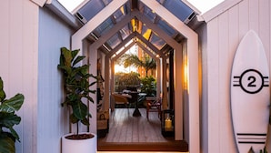 A wooden deck with a table and chairs, a surfboard, and a potted plant.