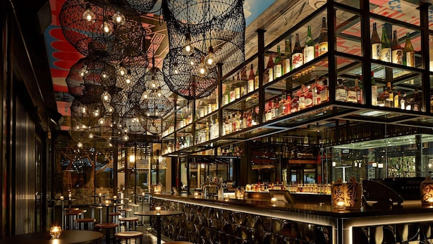 A bar with multiple shelves of liquor bottles, hanging light fixtures, and bar stools.