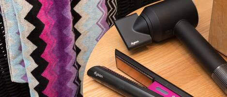 A round wooden table with a Dyson hair dryer and a flat iron.