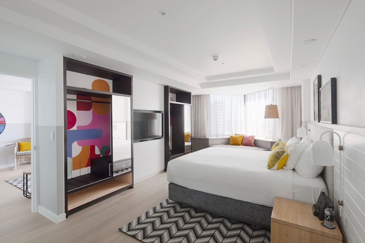 A modern hotel room with a large bed, a TV, and a wardrobe with a colorful geometric design.