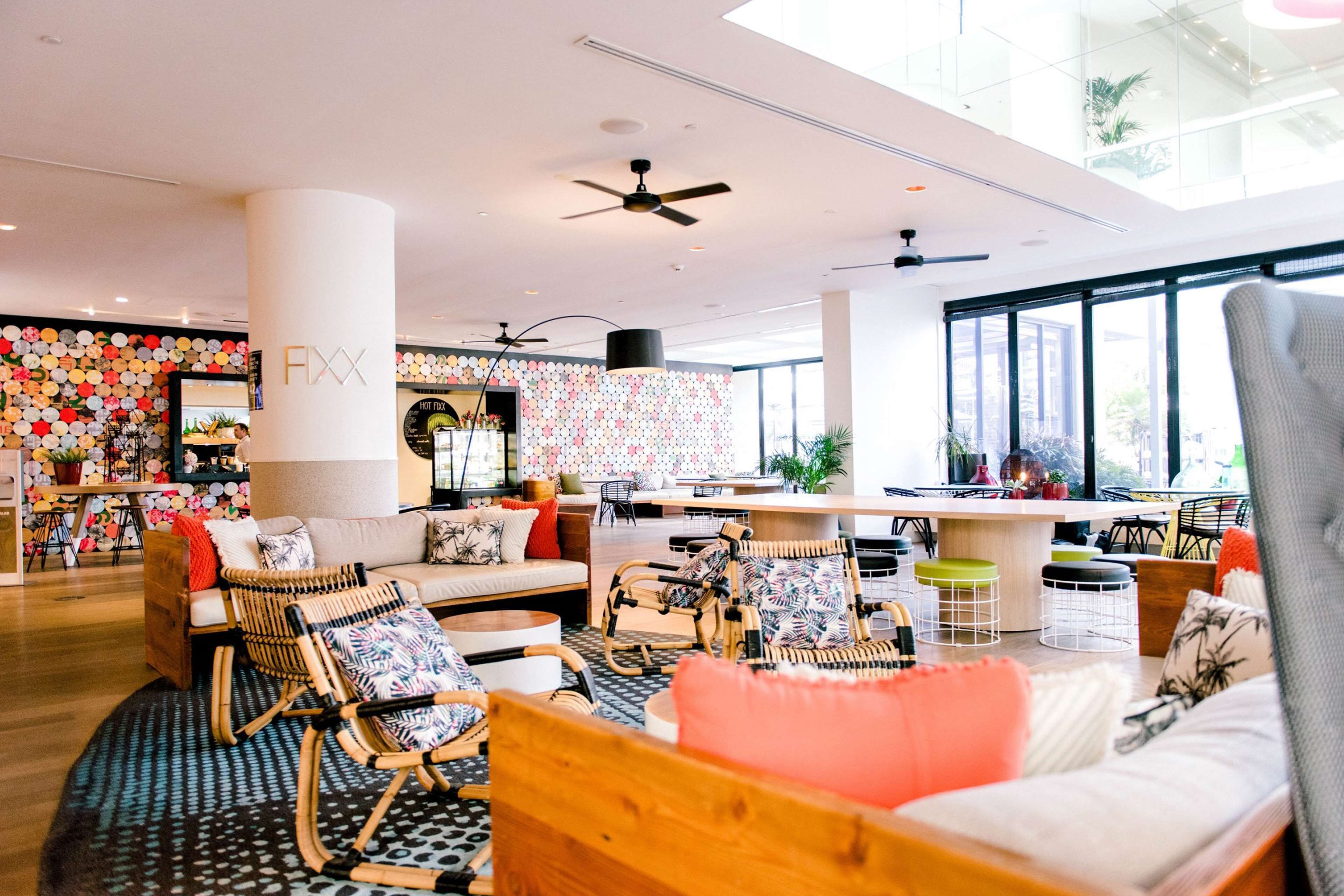 Un vestíbulo de hotel moderno con un área de estar central, un bar y un amplio ventanal con vistas al exterior.