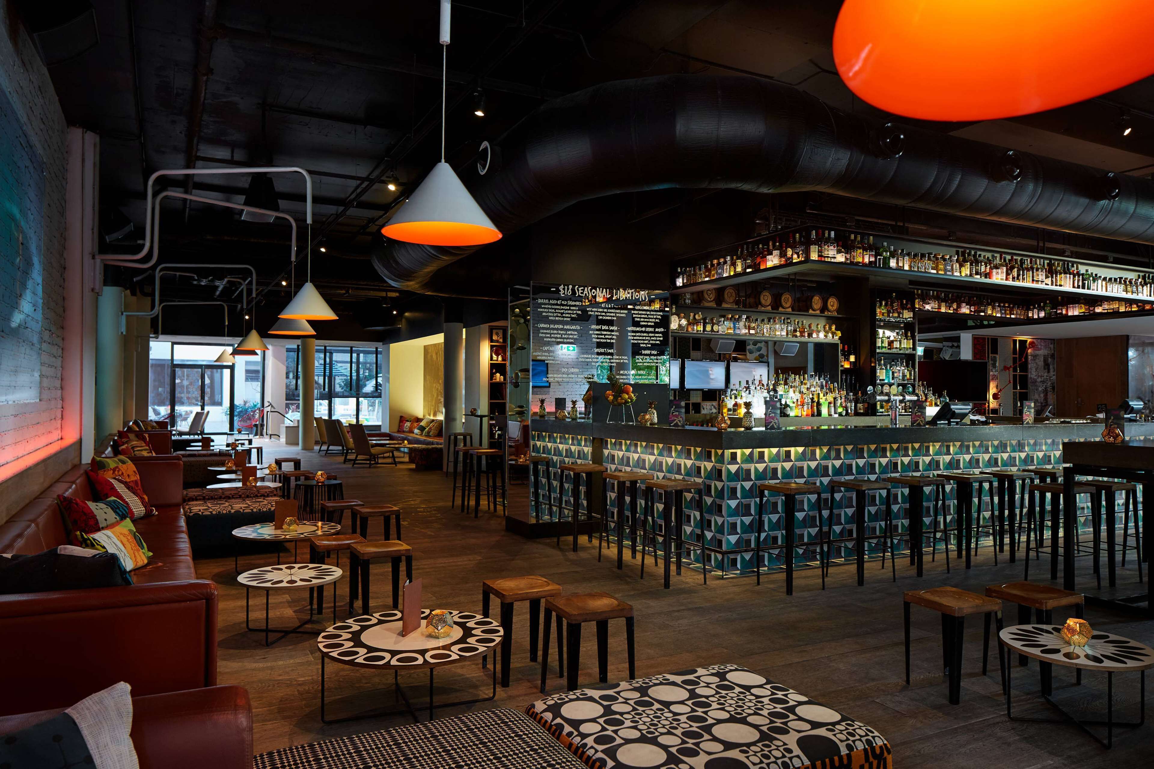 A bar area with a high bar counter, multiple stools, and a variety of bottles.
