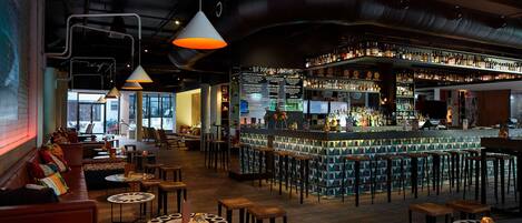 A bar area with a high bar counter, multiple stools, and a variety of bottles.