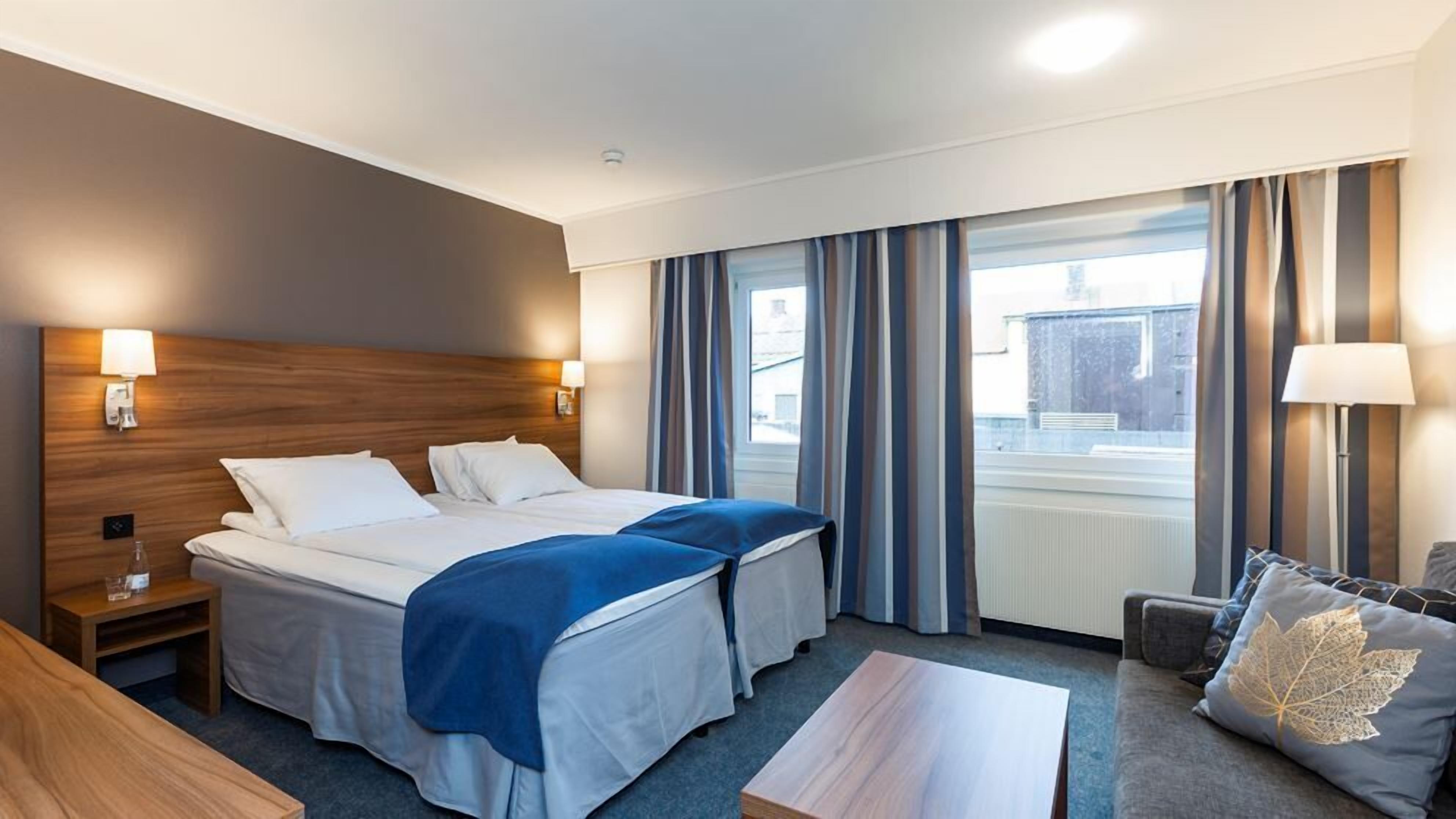 A hotel room with two beds, a desk, a chair, a table, and a view of the outside.