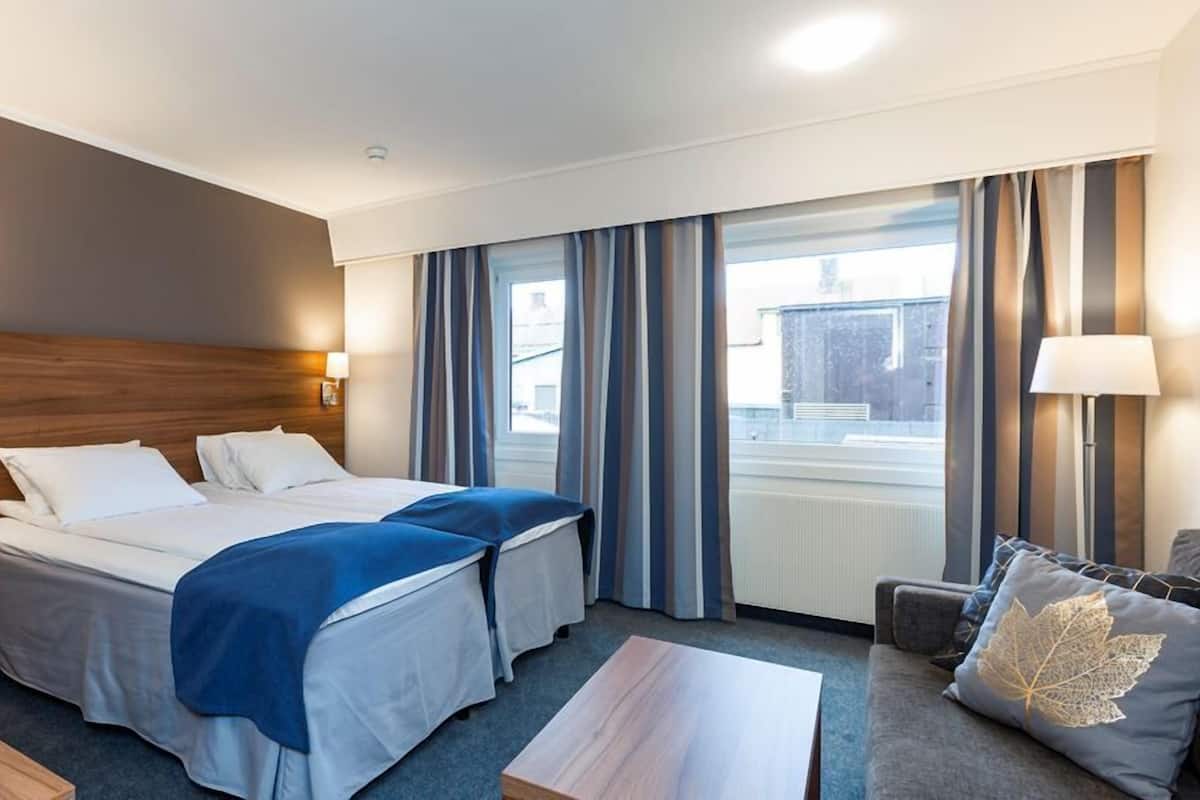 Hotellihuone, jossa on kaksi sänkyä, työpöytä, tuoli, pöytä ja näkymä ulos.