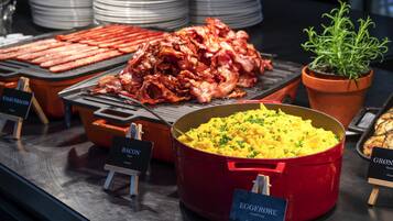 Un bufé con diferentes opciones de comida, incluyendo tocino, huevos revueltos y una olla roja de puré de papas.