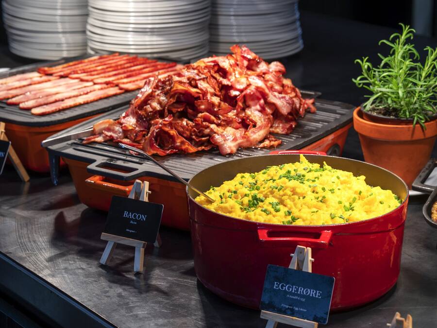 A buffet with various food items including bacon, scrambled eggs, and a red pot of mashed potatoes.