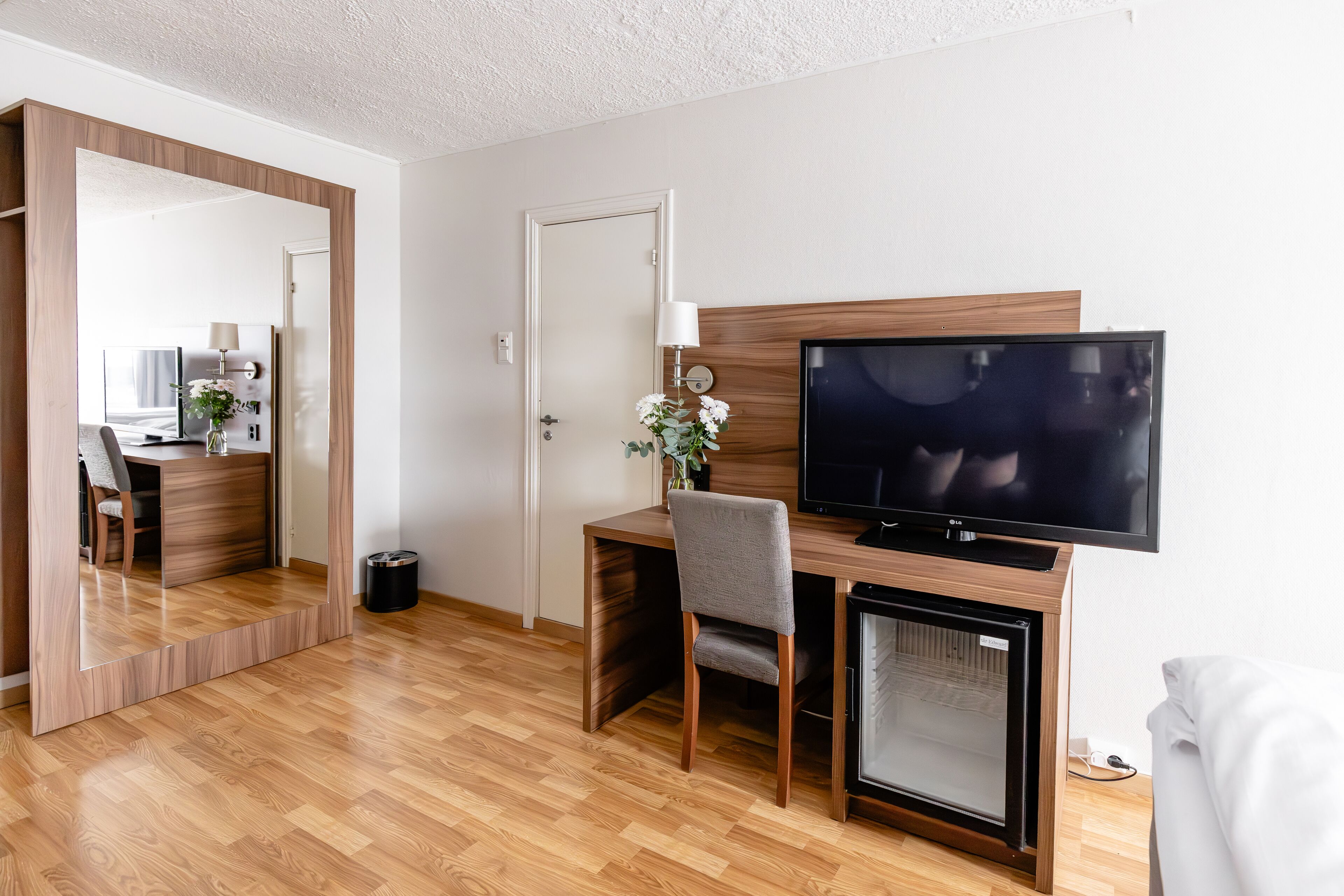 Ett modernt hotellrum med ett skrivbord i trä, en tv och en spegel.