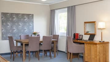 A dining area with a wooden table and chairs, a window with curtains, a desk with a laptop, and a mirror.