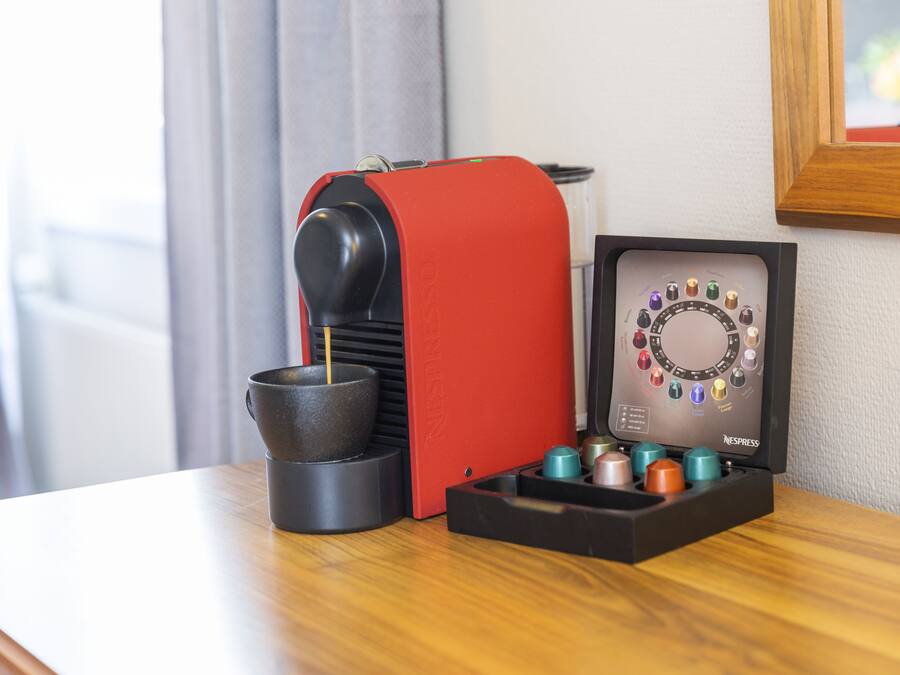 A Nespresso coffee machine with a red base, a coffee pod holder, and a Nespresso capsule display.