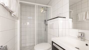 A modern bathroom with white tiles, a toilet, a shower with a glass door, and a vanity with a mirror.