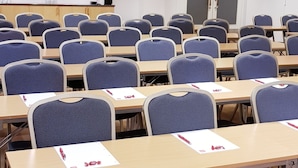 Ein Konferenzraum mit Tischen und Stühlen, einem großen Spiegel an der Wand und einer Tür mit Lampe darüber.