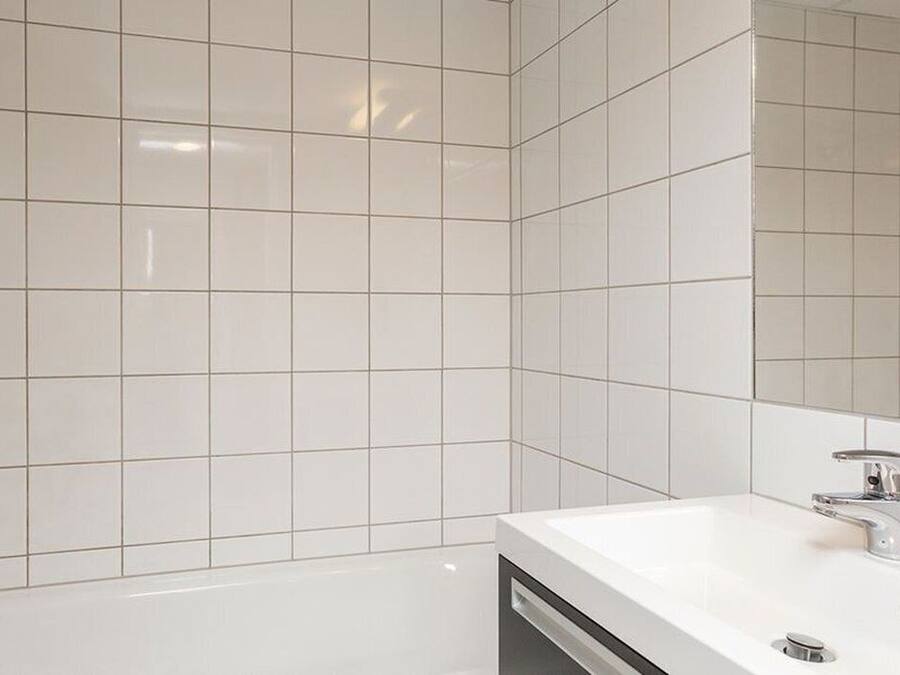 Un baño con baldosas blancas, una bañera, un lavamanos con grifo y un cabezal de ducha.