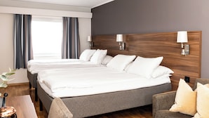Ein Hotelzimmer mit einem großen Bett, zwei Nachttischlampen, einem Holzkopfteil und Blick ins Freie durch das Fenster.