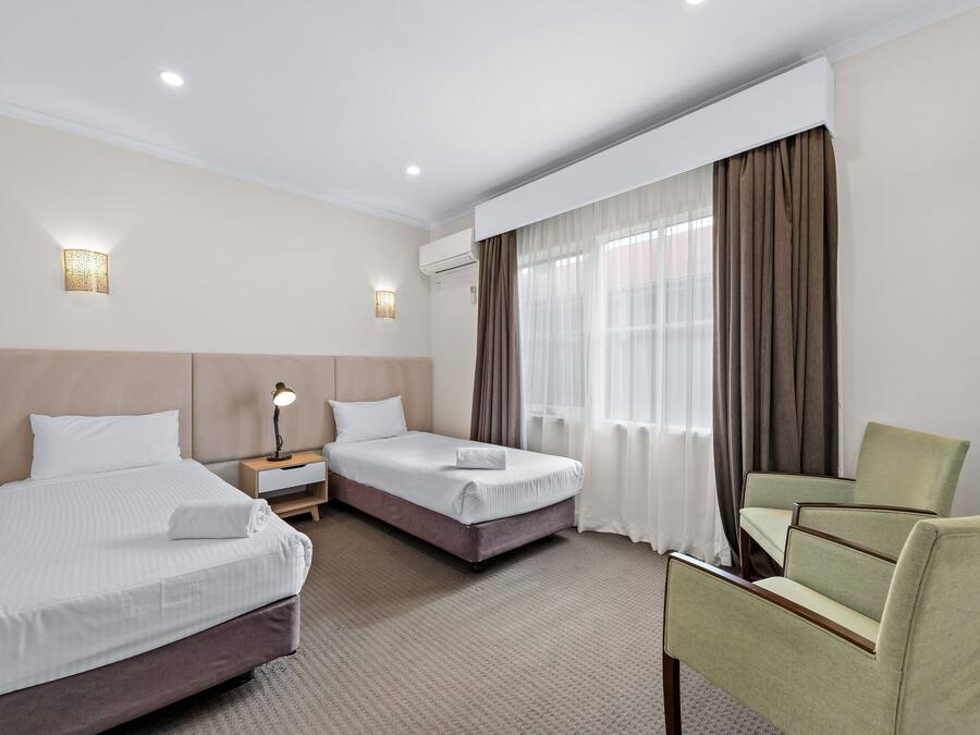 A hotel room with two beds, a chair, a nightstand, and a lamp.