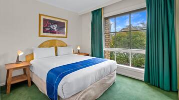 Un cuarto de hotel ordenado con una cama grande, una obra de arte enmarcada en la pared, una ventana con cortinas y vistas a zonas verdes.