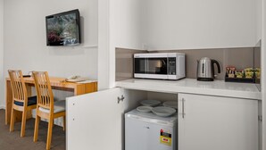 A compact kitchenette with a microwave, kettle, and small refrigerator. There is a wooden table with two chairs and a TV mounted on the wall. - Rowville International Hotel (Rowville)