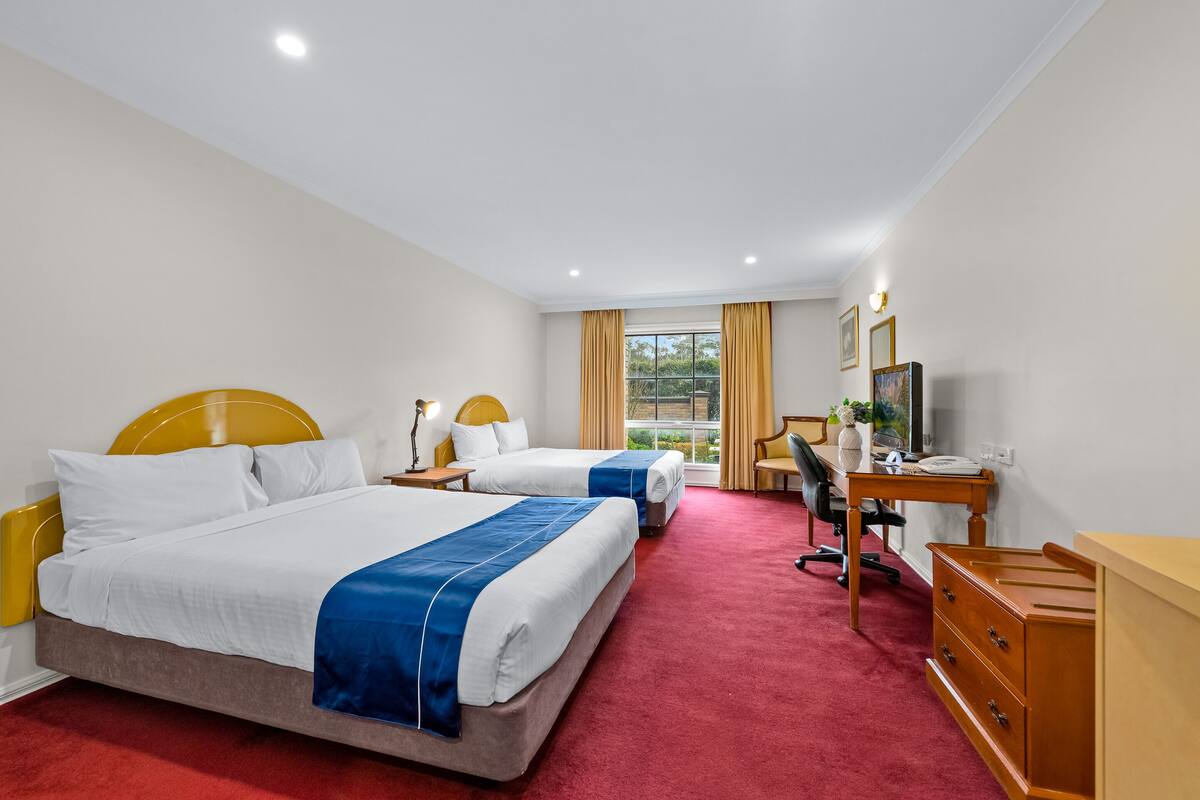 Habitación de hotel con dos camas, un escritorio, una silla y un televisor.