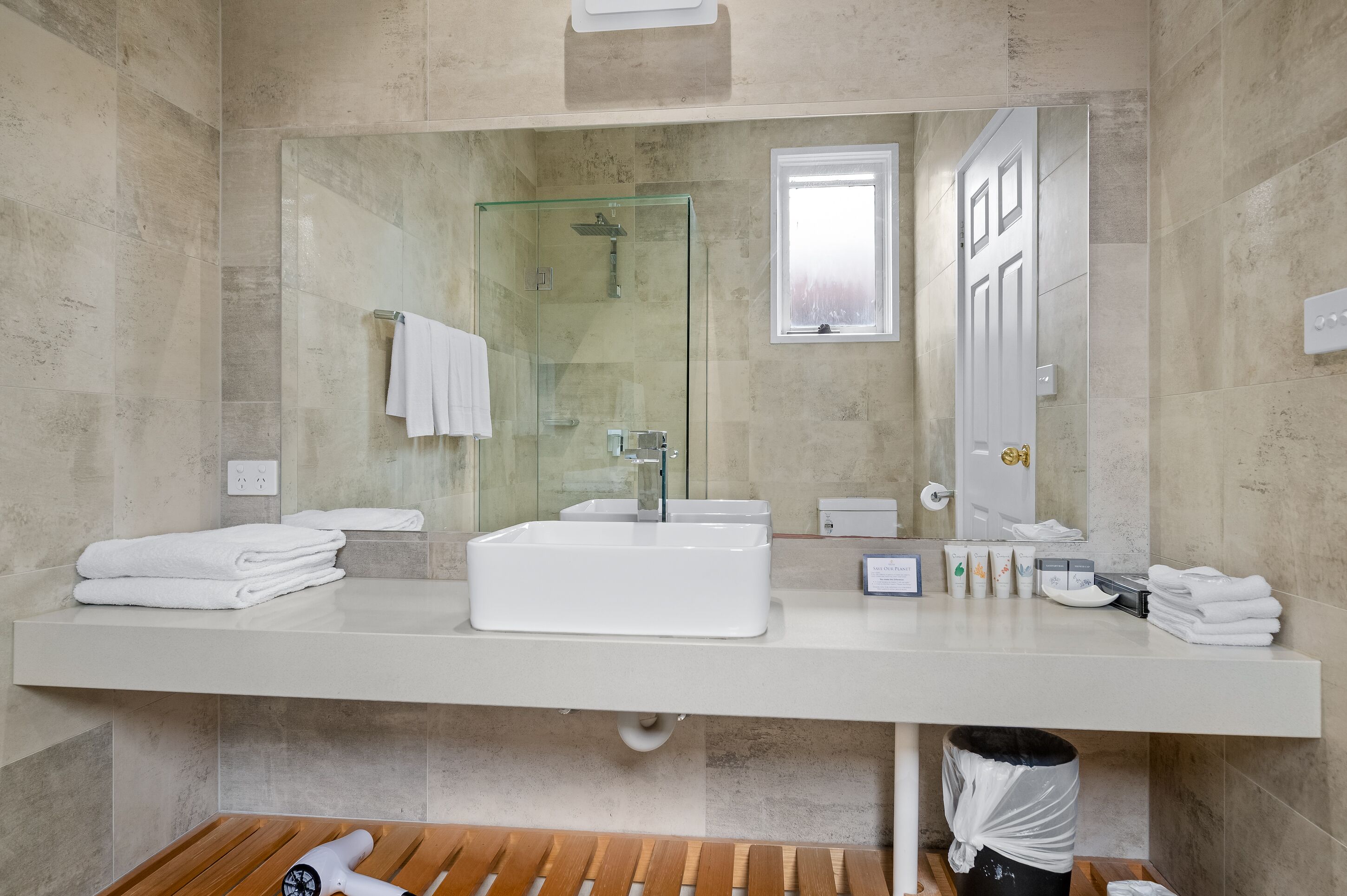 A modern bathroom with a large mirror, a glass-enclosed shower, and a white sink.