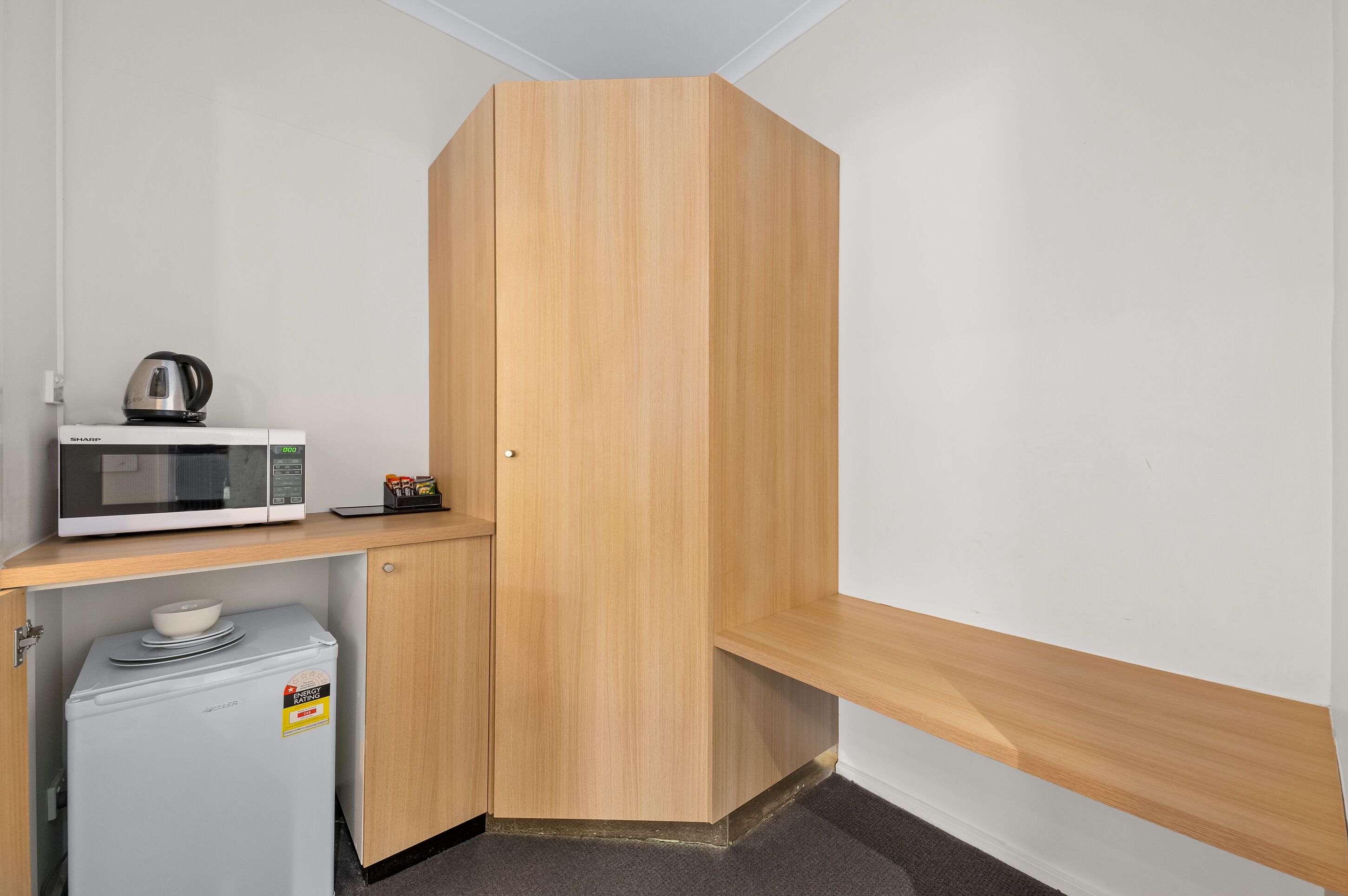 Una kitchenette compacta con microondas, hervidor y refrigerador pequeño.
