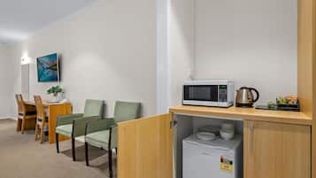 A compact kitchenette with a microwave, a small refrigerator, and a coffee maker. There is a dining area with a table and chairs, and a painting on the wall.