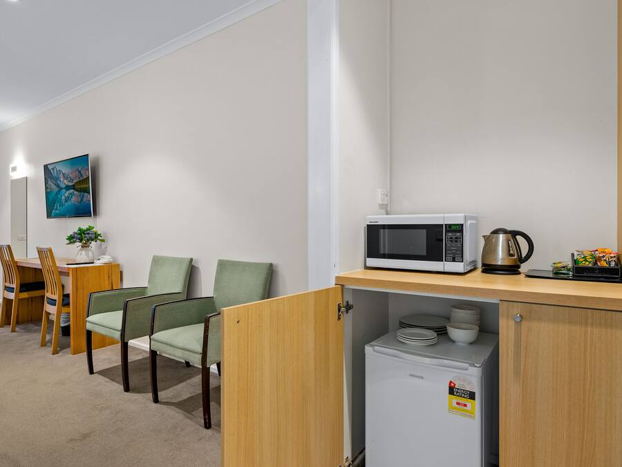 A compact kitchenette with a microwave, a small refrigerator, and a coffee maker. There is a dining area with a table and chairs, and a painting on the wall.