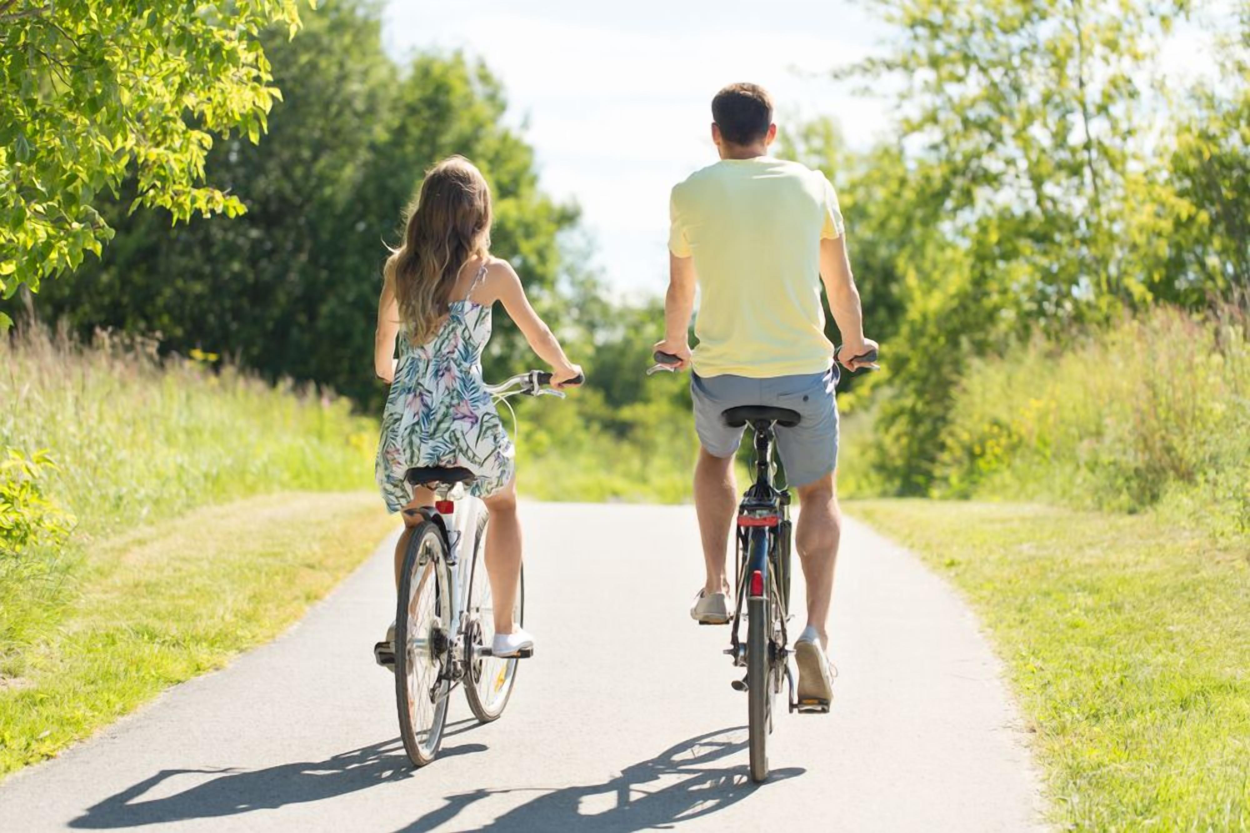 Two people riding bicycles on a paved path surrounded by greenery.