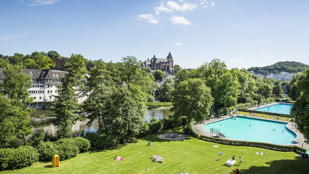 A large swimming pool surrounded by a well-maintained lawn, a small boat, and a castle in the background. - Best Western Hotel Wetzlar (Wetzlar)