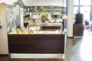 Una barra de desayuno con diversas opciones de comida y bebida, un centro de mesa decorativo con plantas, y un mural panorámico de fondo.