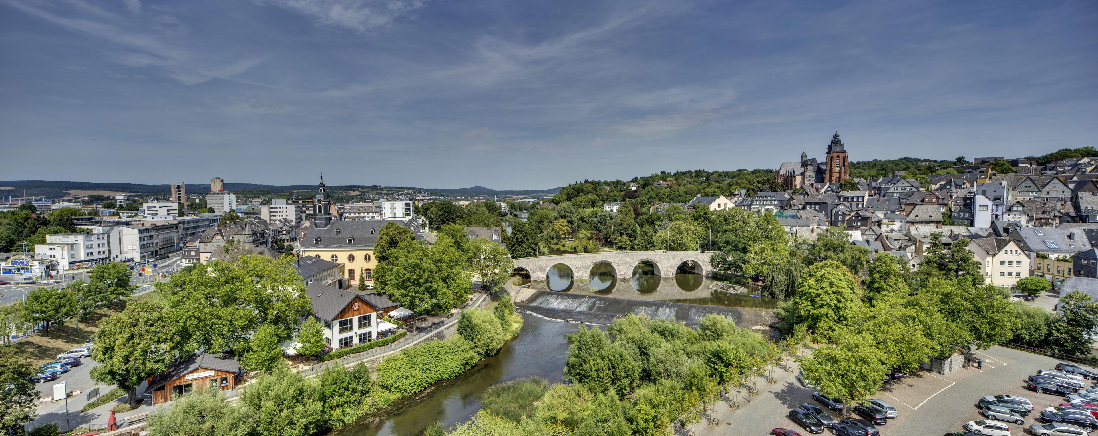 A riverside town with a historic bridge, modern buildings, and a prominent church tower.