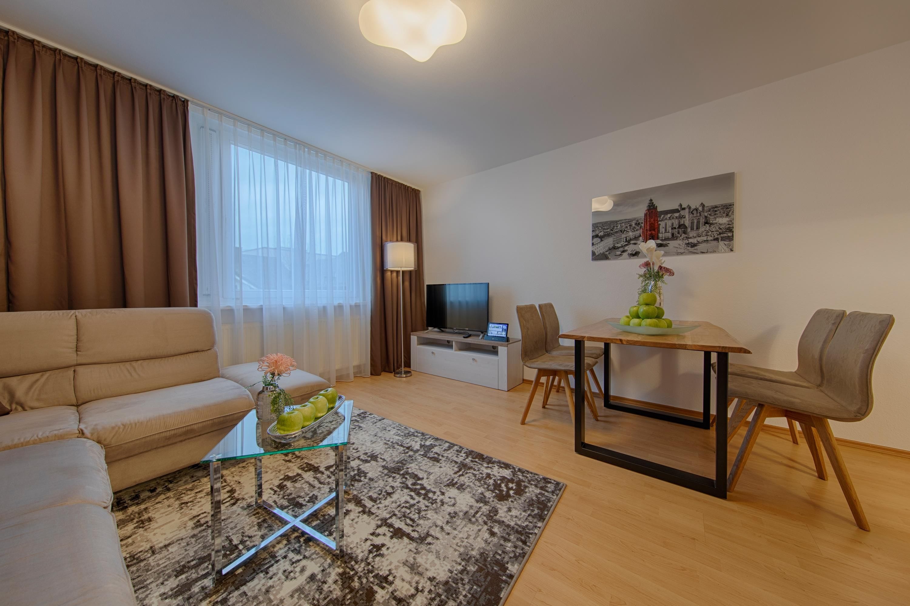 Un salon moderne comprenant un canapé, une table basse en verre, une table à manger avec des chaises, un téléviseur à écran plat et un tableau accroché au mur.