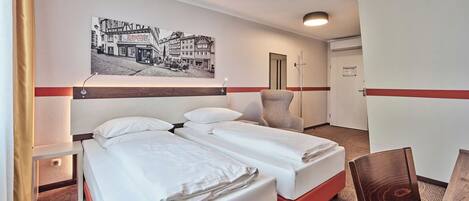 Habitación de hotel con dos camas, un escritorio, una silla, un cuadro en la pared y una puerta.